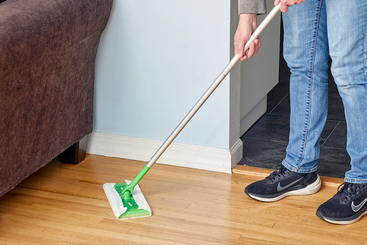 Жінка використовує швабру Swiffer для сухого прибирання дерев'яної підлоги.